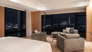 A modern hotel room with a large bed, two armchairs, a small table, and large windows offering a city view at night. - Taipei Marriott Hotel (Taipei)