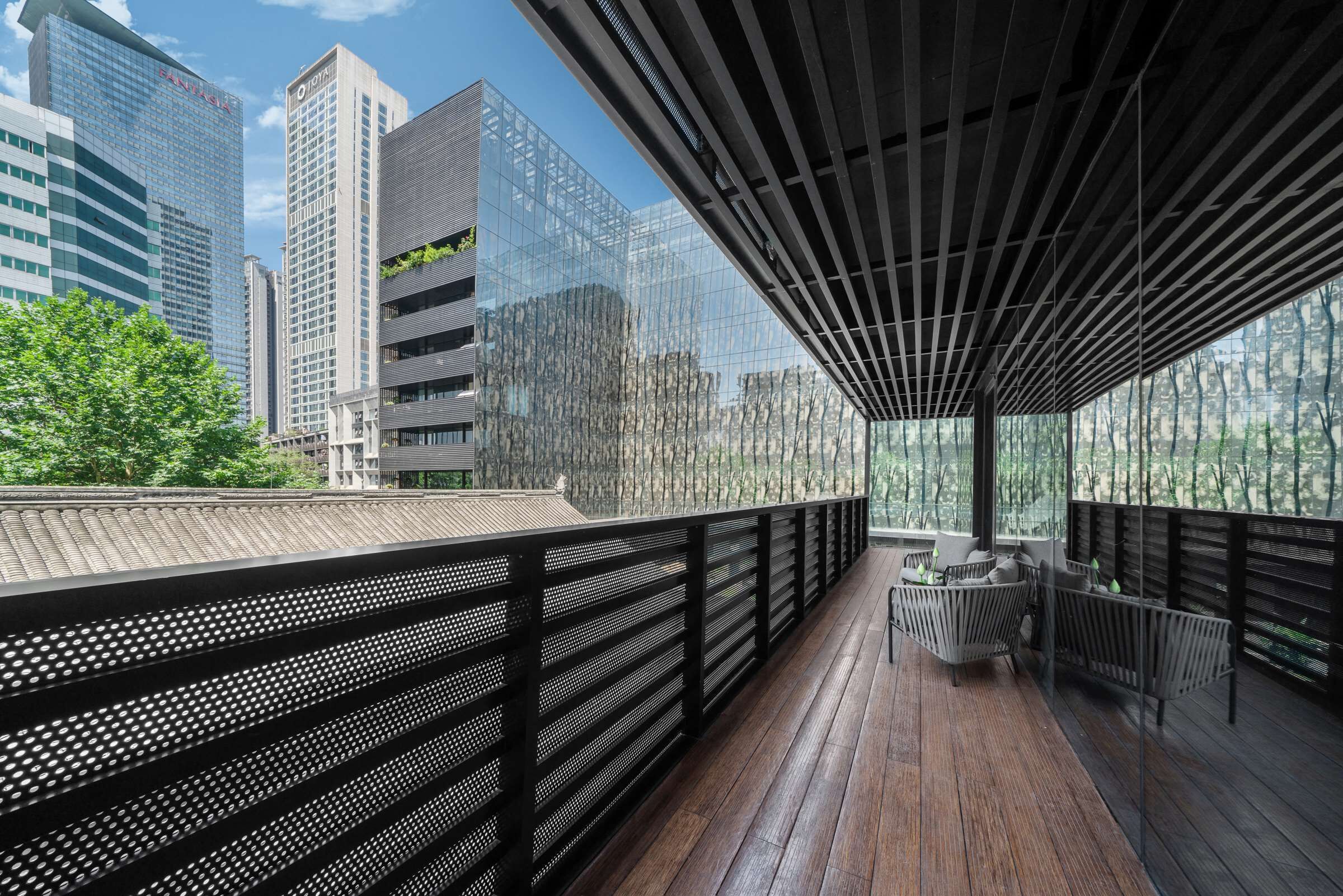 Una terraza moderna en la azotea con piso de madera, barandas de metal negro y un área de estar con cojines.