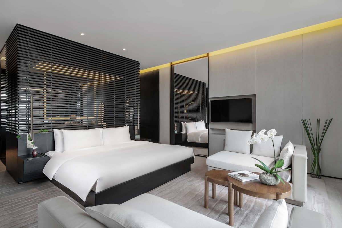 A modern hotel room with a large bed, a sofa, a coffee table, and a TV.
