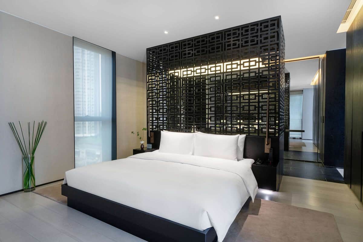 A modern bedroom with a large bed, a decorative black partition, and a view of the city.