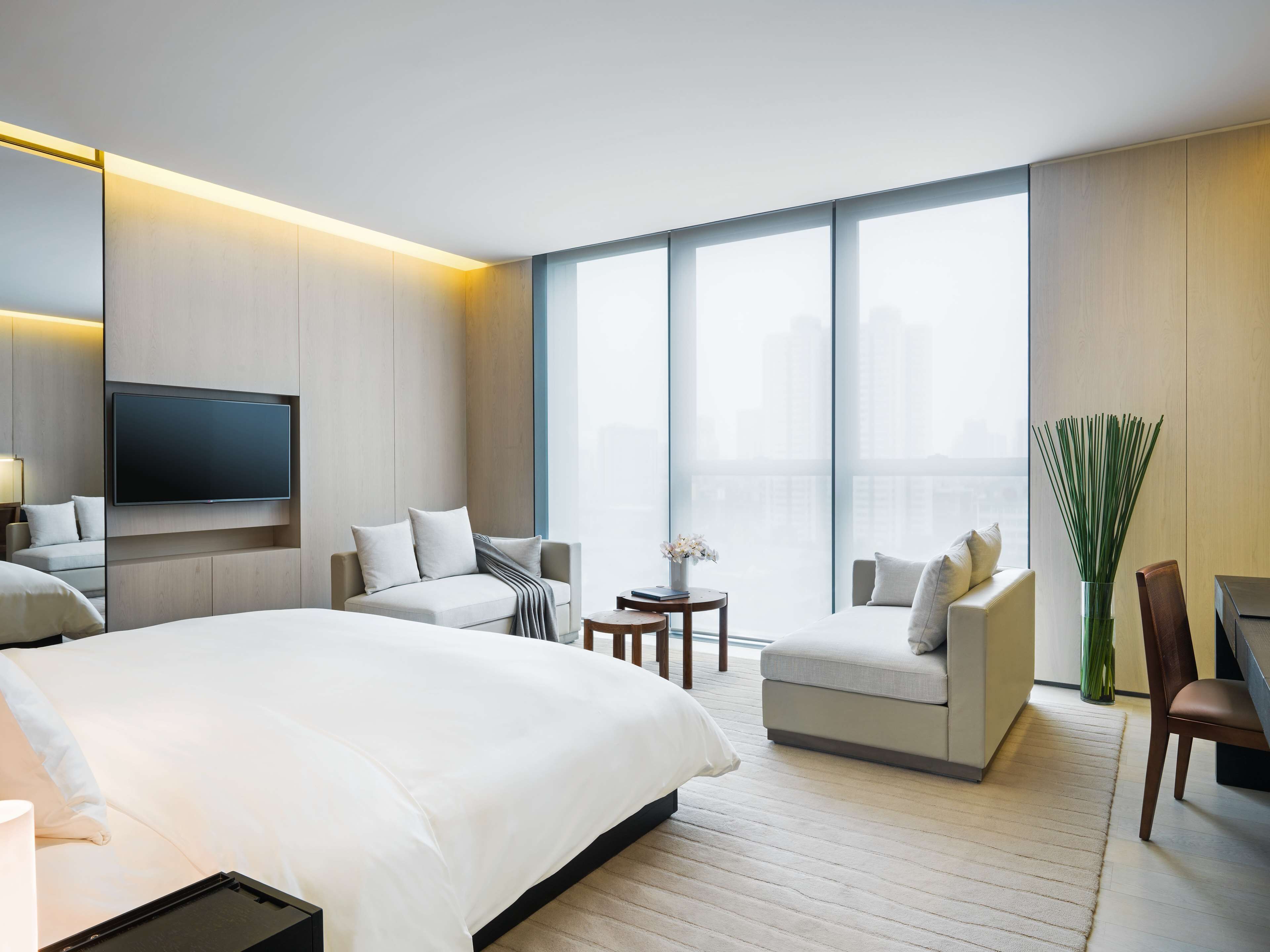 A modern hotel room with a large bed, a sofa, a desk, and a television mounted on the wall.