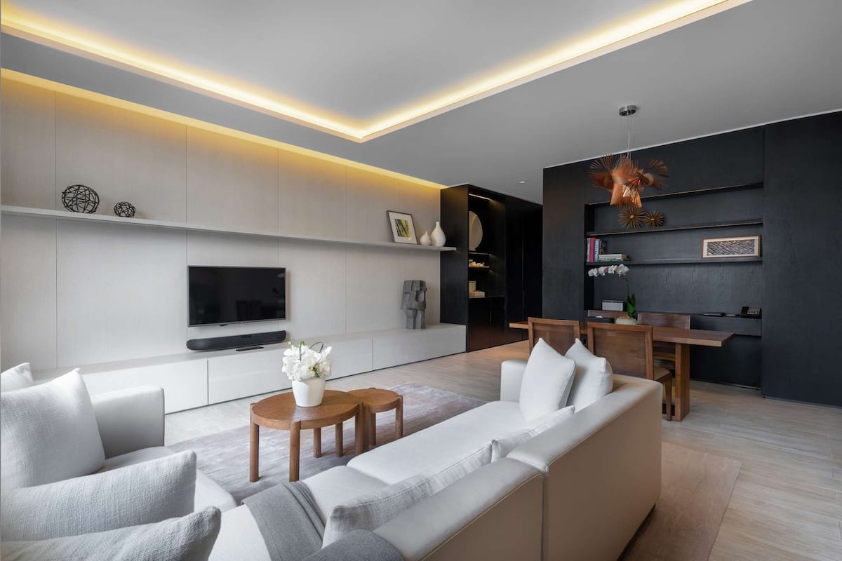A modern living room with a flat-screen TV, a sofa, a coffee table, and a dining area with a wooden table and chairs.