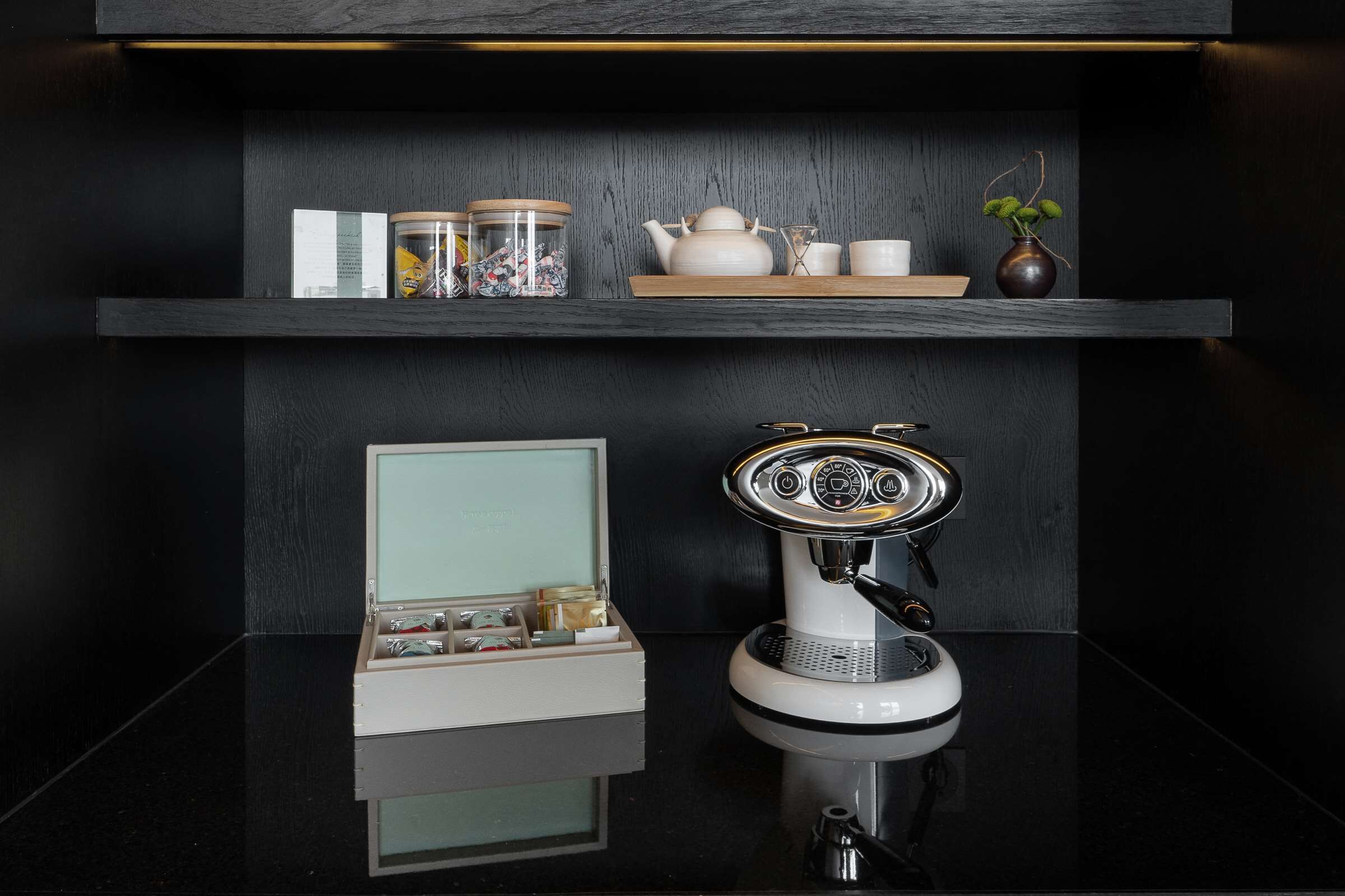 A modern kitchen with a coffee machine, a tea set, and a small shelf with decorative items.