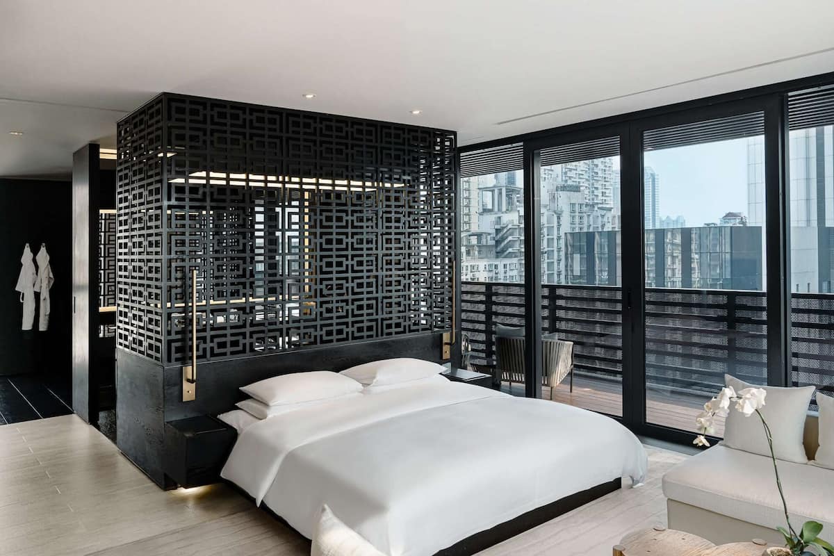 A modern bedroom with a large bed, a decorative black partition, and a city view through large windows.
