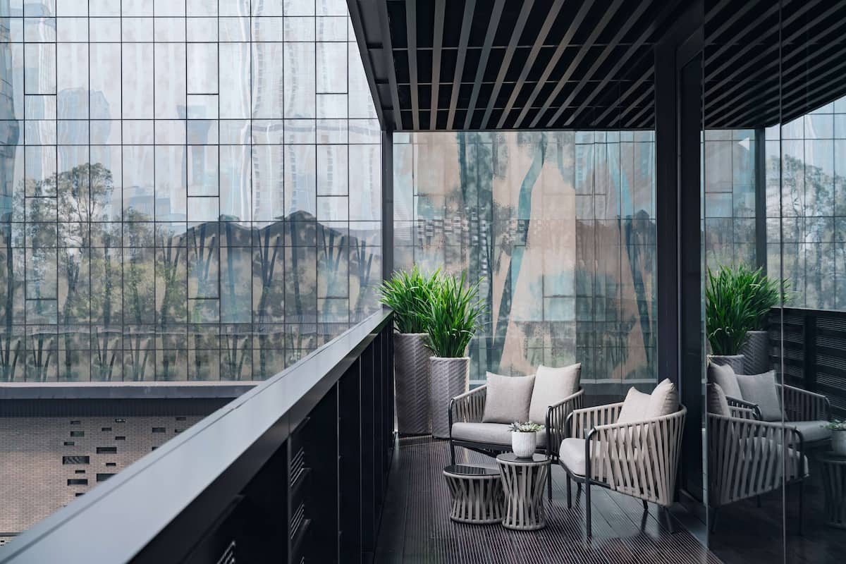 A modern balcony with wicker furniture, a potted plant, and a cityscape view through large windows.