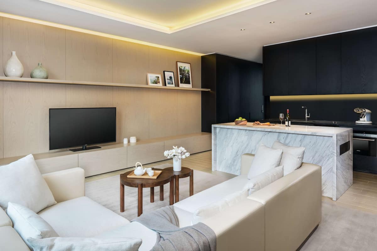 A modern living room with a large flat-screen TV, a sofa, a coffee table, and a marble island with a sink and counter.