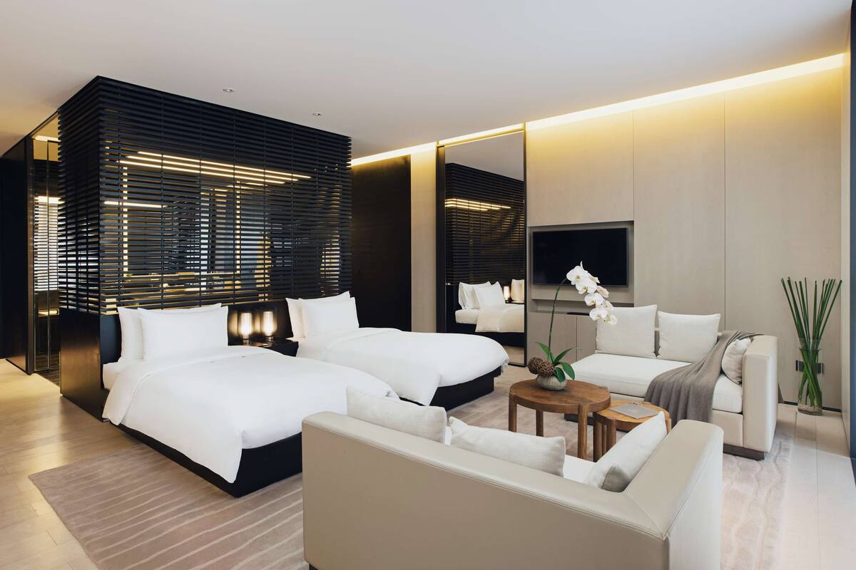 A modern hotel room with a large bed, a sofa, a coffee table, and a TV.