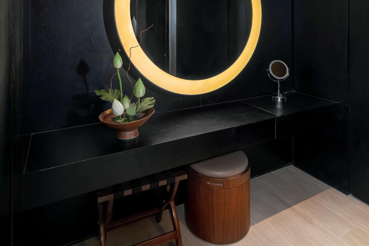 A modern bathroom with a large mirror, a small stool, and a trash can.