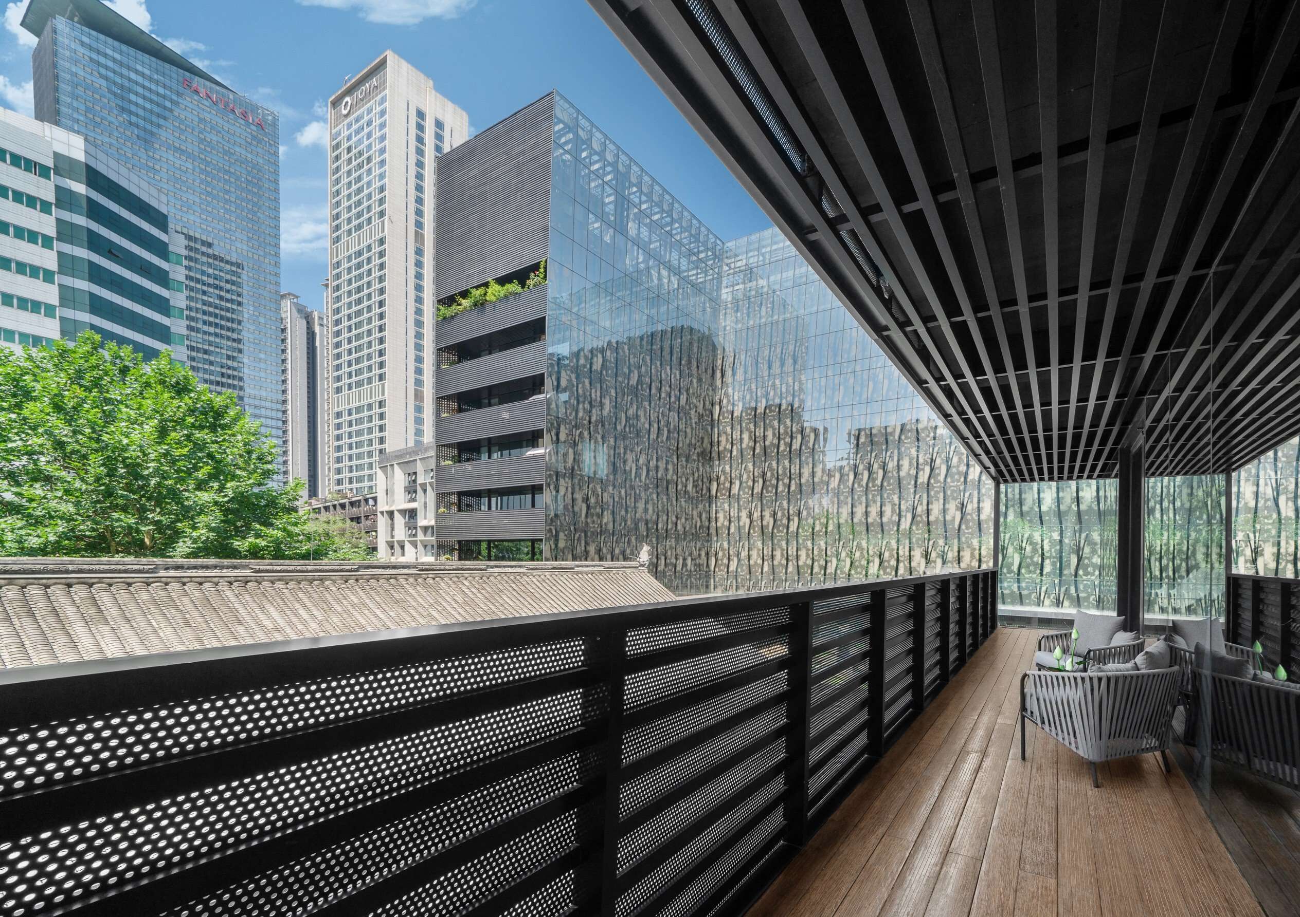A modern building with a glass facade, a rooftop terrace with a wooden deck, and a seating area with cushions.