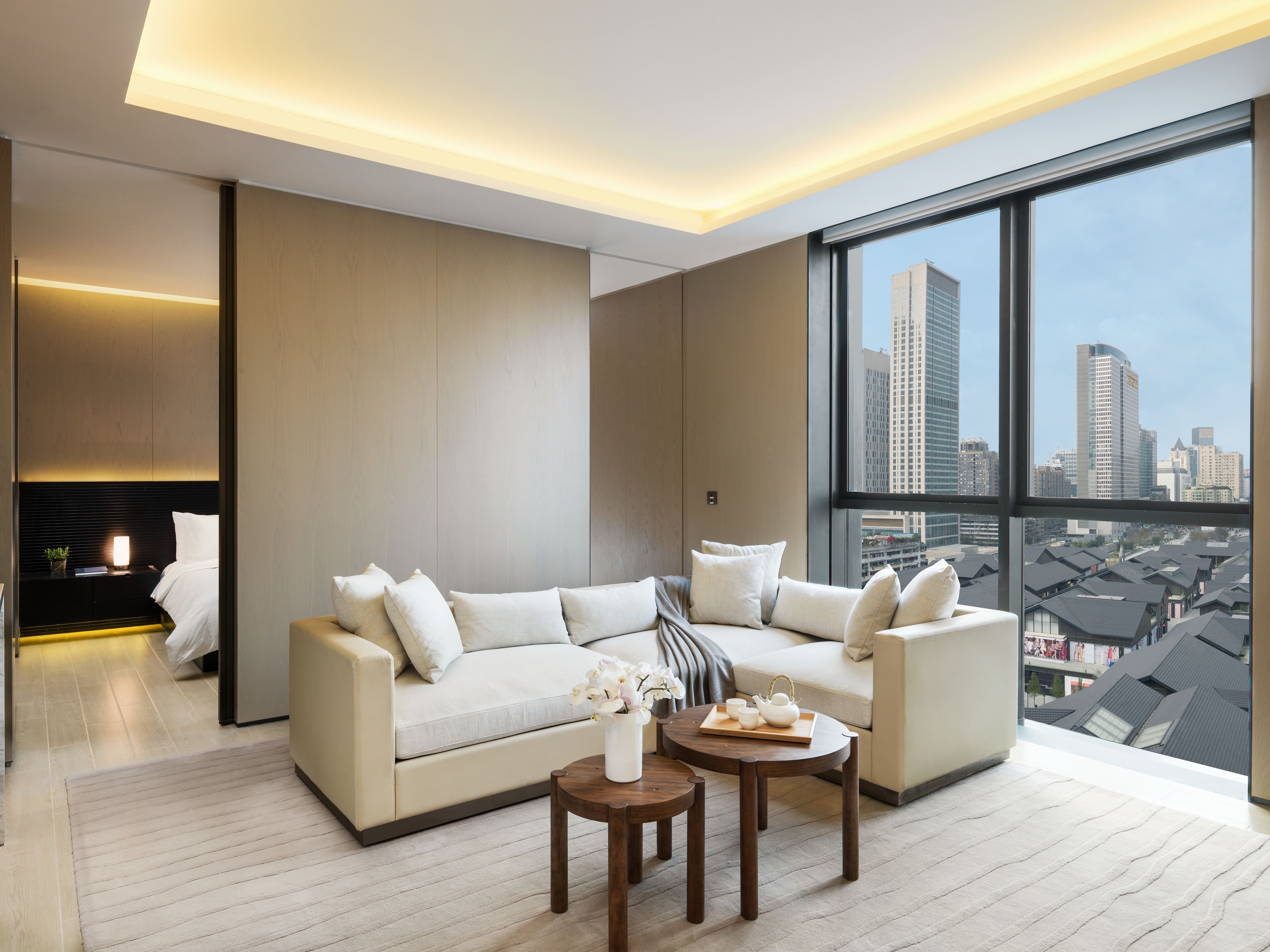 A modern living room with a large sofa, a coffee table, and a view of a cityscape through large windows.