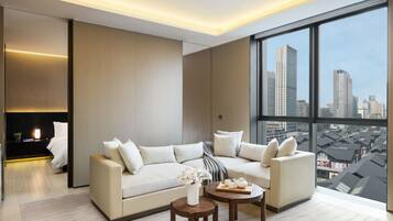 A modern living room with a large sofa, a coffee table, and a view of a cityscape through large windows.