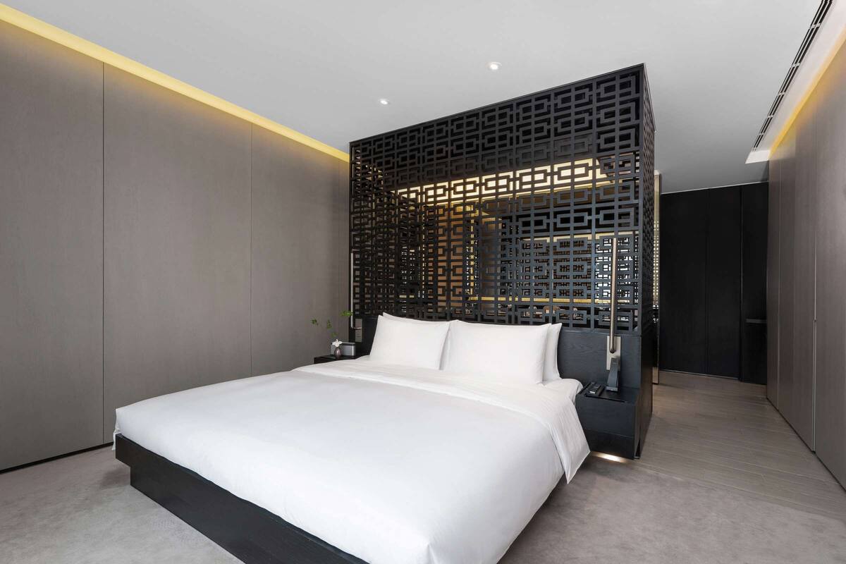 A modern bedroom with a large bed, a decorative black partition, and recessed ceiling lighting.