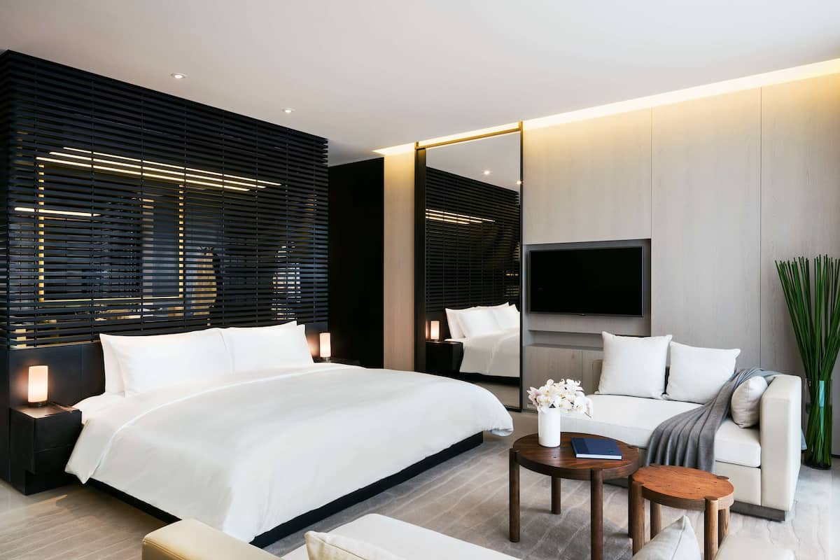 A modern hotel room with a large bed, a sofa, a TV, and a small table.