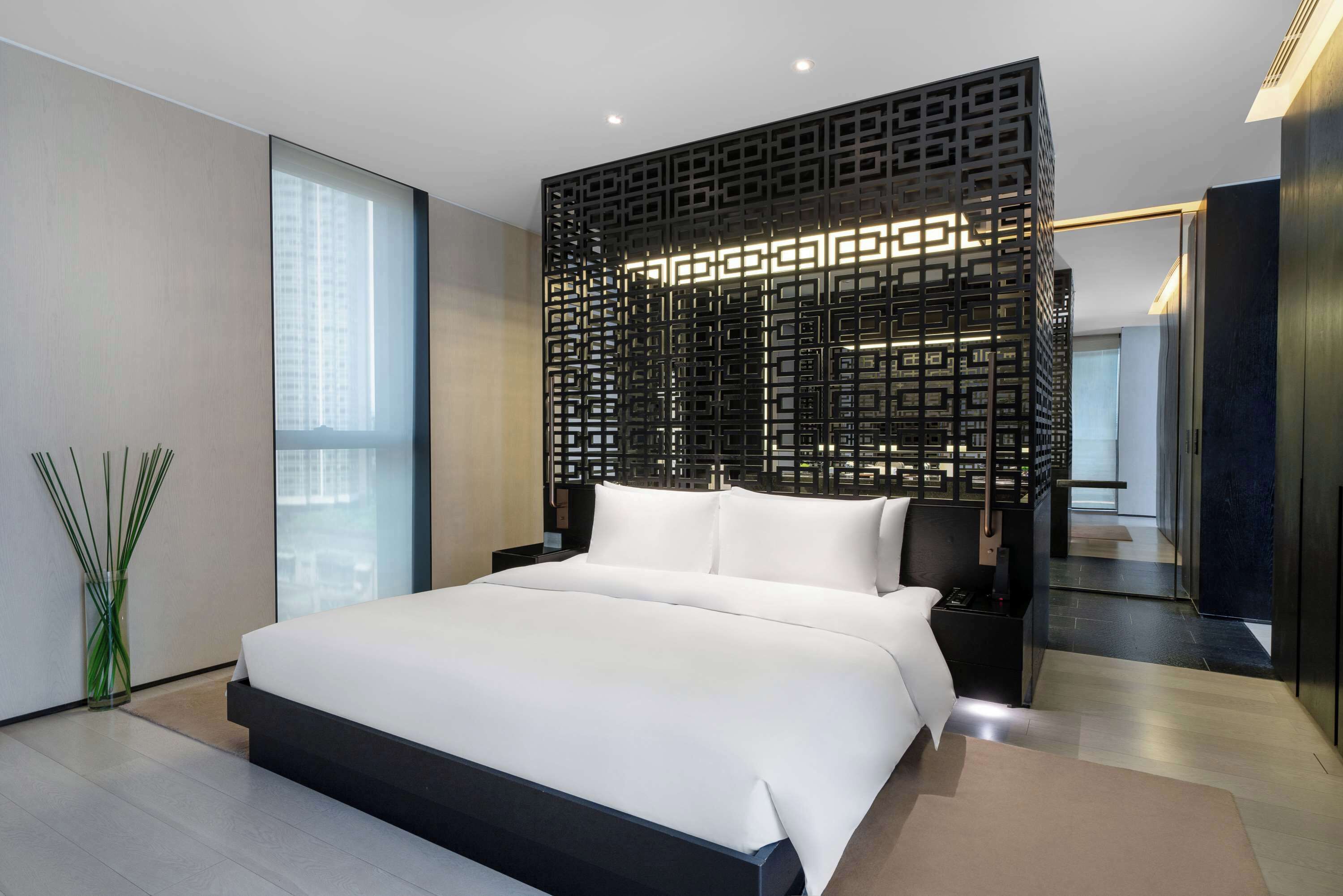 Una habitación de hotel moderna con una cama grande, un panel decorativo negro y vistas de la ciudad.
