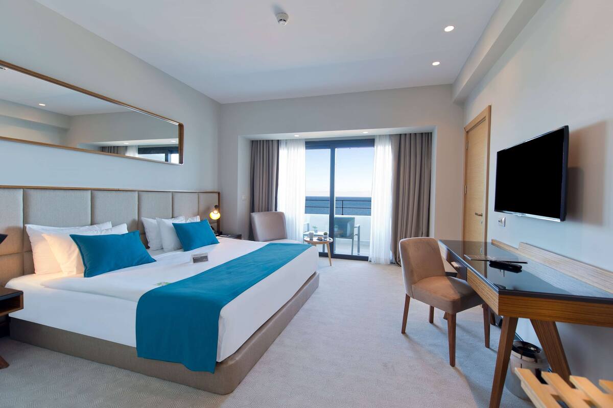 Une chambre d’hôtel avec un grand lit, un bureau, une chaise, une télévision et un balcon avec vue.