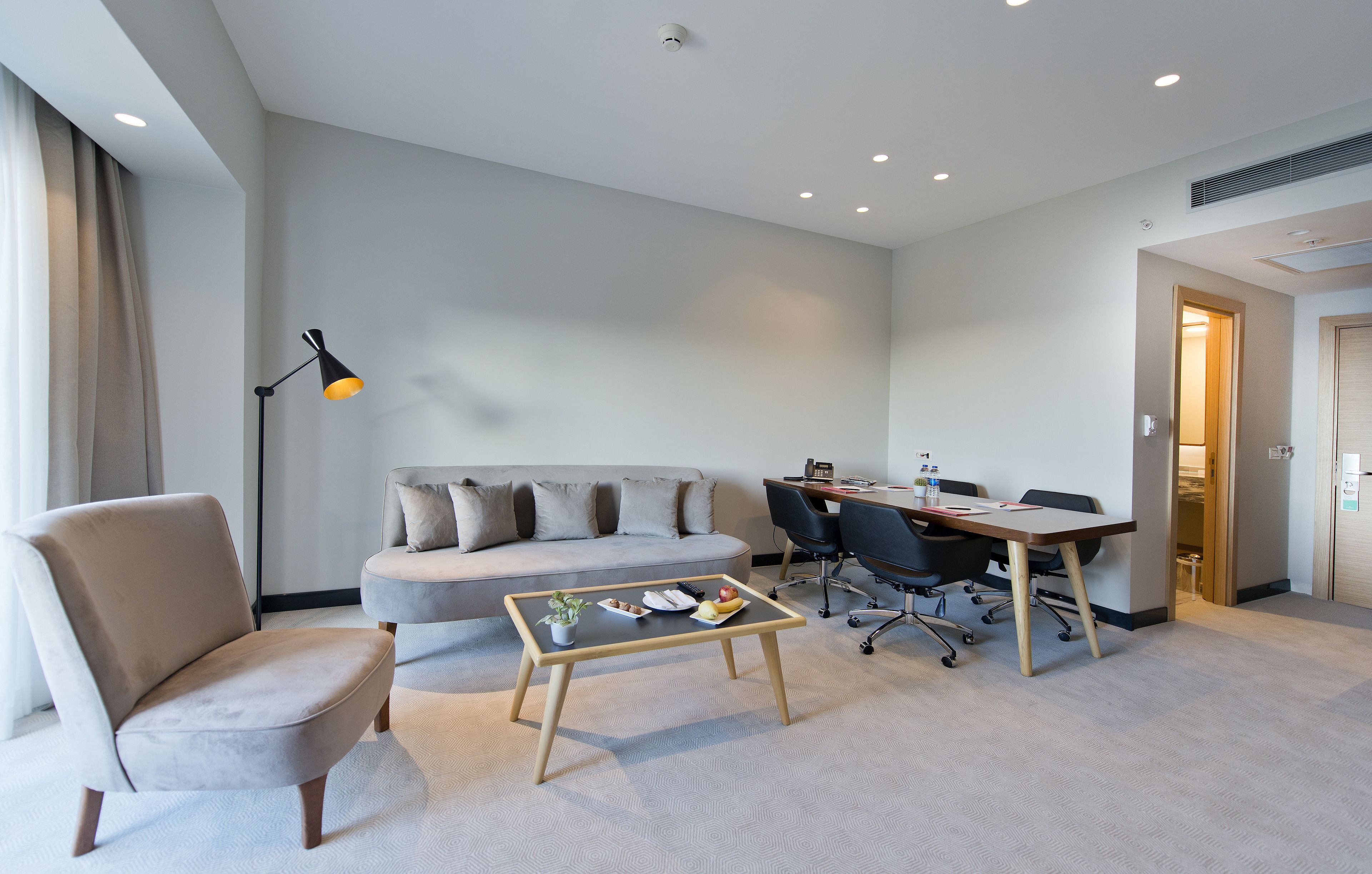 Una habitación de hotel moderna con sofá, sillón, mesa de comedor y una pequeña mesa de centro.