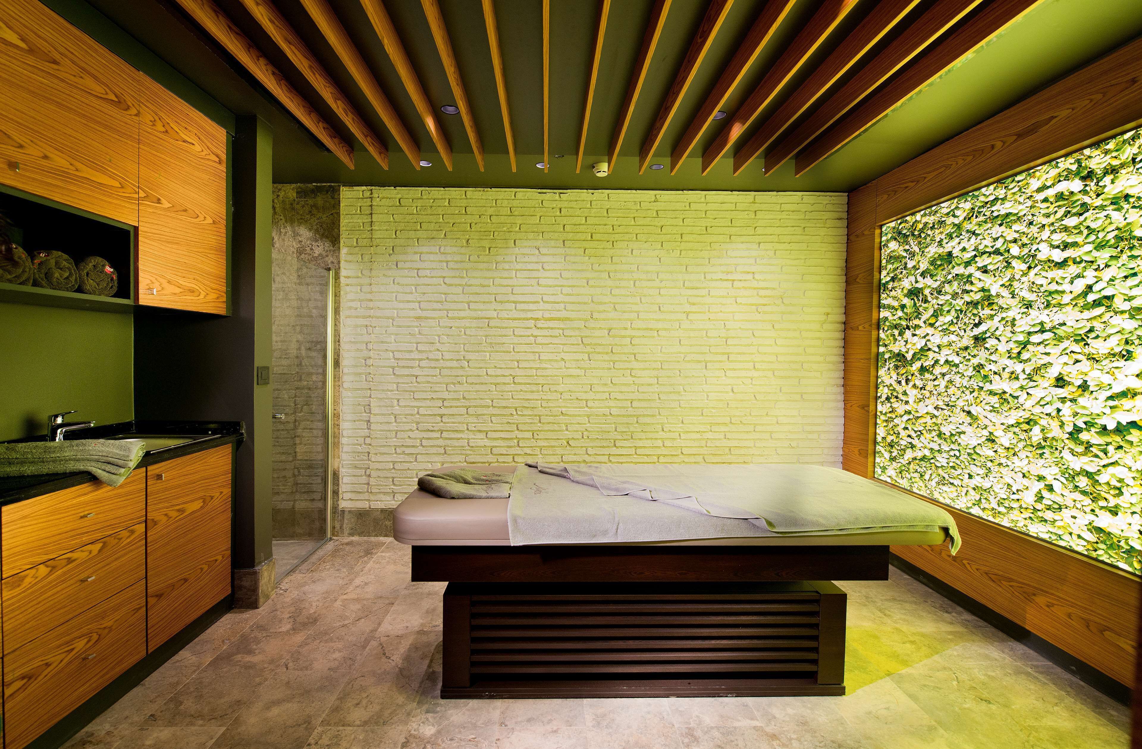 Una moderna sala spa con una panca in legno, una parete in mattoni e una parete verde decorata con un motivo a foglie.