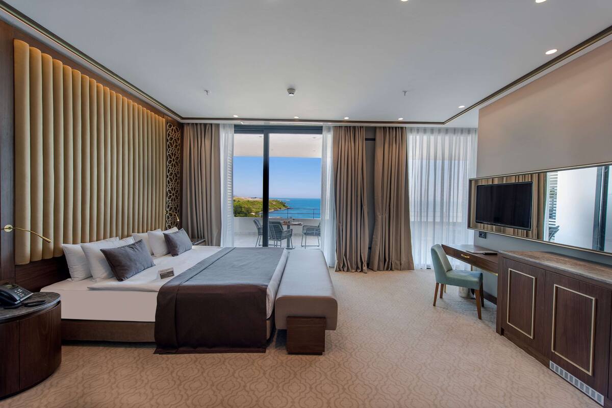 Une chambre d’hôtel équipée d’un lit, d’un bureau, d’une télévision et d’un balcon avec vue sur la mer.