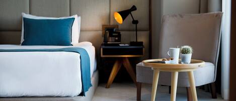 Una habitación de hotel con una cama, una mesita de noche, una lámpara, una silla y una pequeña mesa con una taza y una planta.