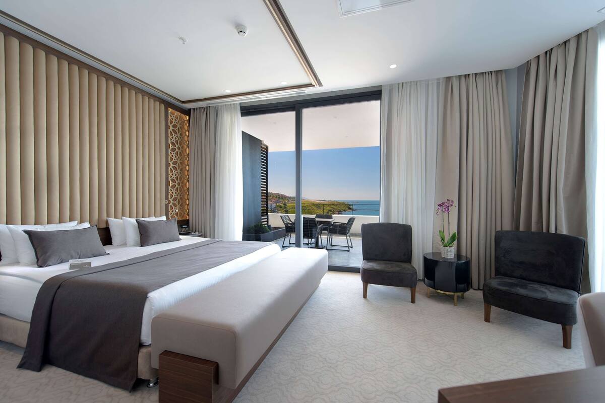 Une chambre d’hôtel moderne dotée d’un grand lit, d’un coin salon avec vue et d’un balcon offrant un panorama agréable.