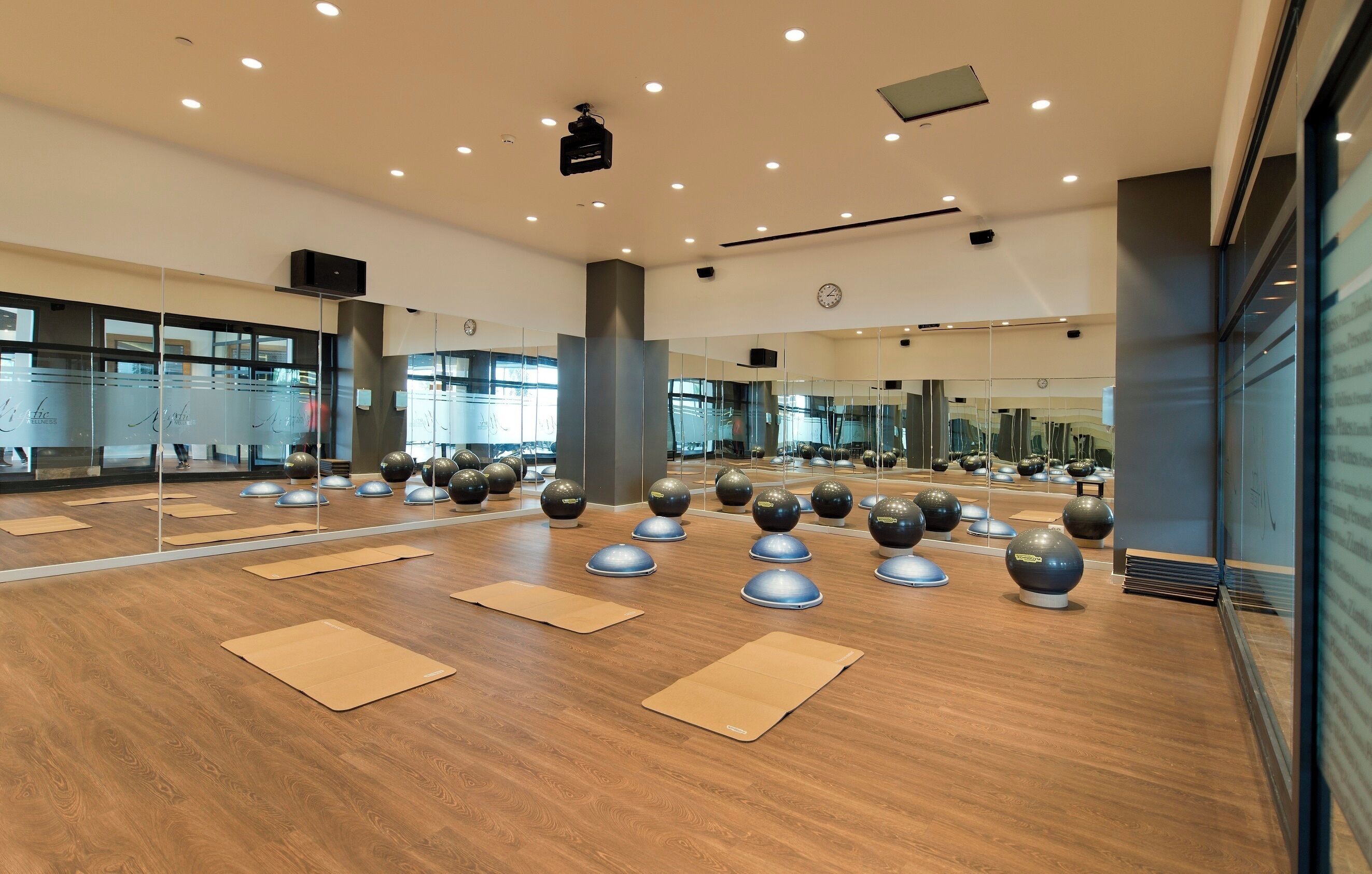 Une salle de sport moderne équipée de matériel d’exercice, de miroirs et d’un plancher en bois.