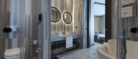 A modern bathroom with a large mirror, two sinks, a toilet, and a bathtub.