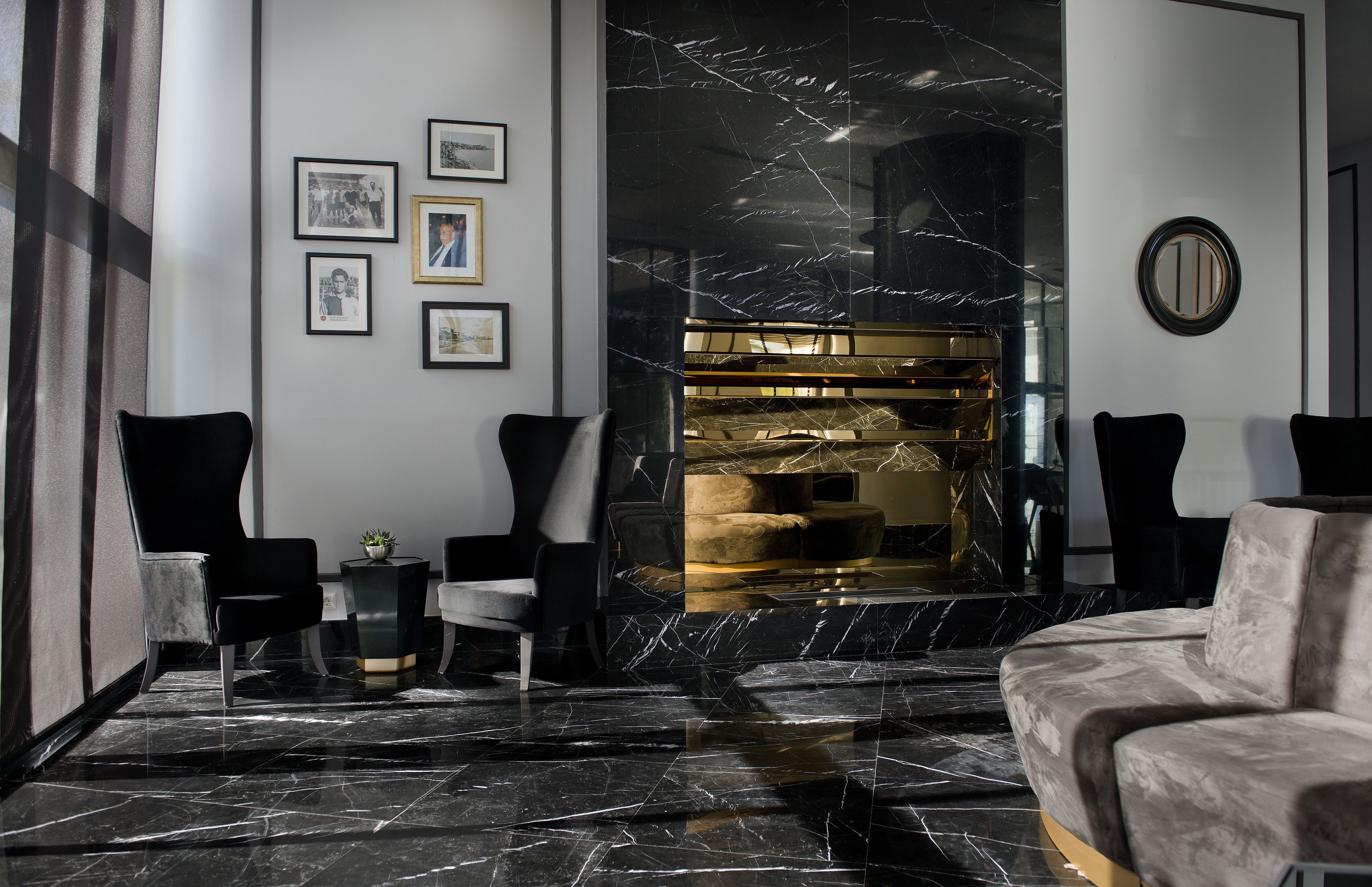 A modern lobby with a marble floor, black and white chairs, a plush sofa, and a fireplace with a gold accent.