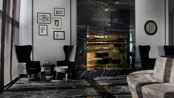 A modern lobby with a marble floor, black and white chairs, a plush sofa, and a fireplace with a gold accent.