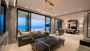 A modern living room with a large sofa, a coffee table, and a dining area with chairs. There is a large window providing a view of the ocean. - Ramada Plaza by Wyndham Trabzon (Trabzon)