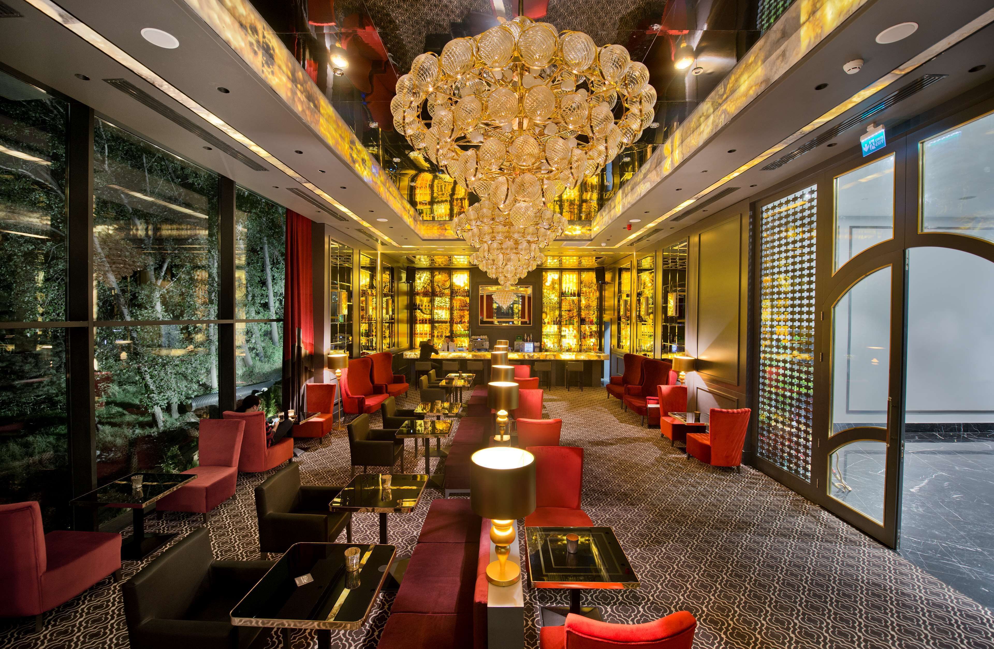 A luxurious hotel lobby with a grand chandelier, comfortable seating, and a view of the outdoors through large windows.