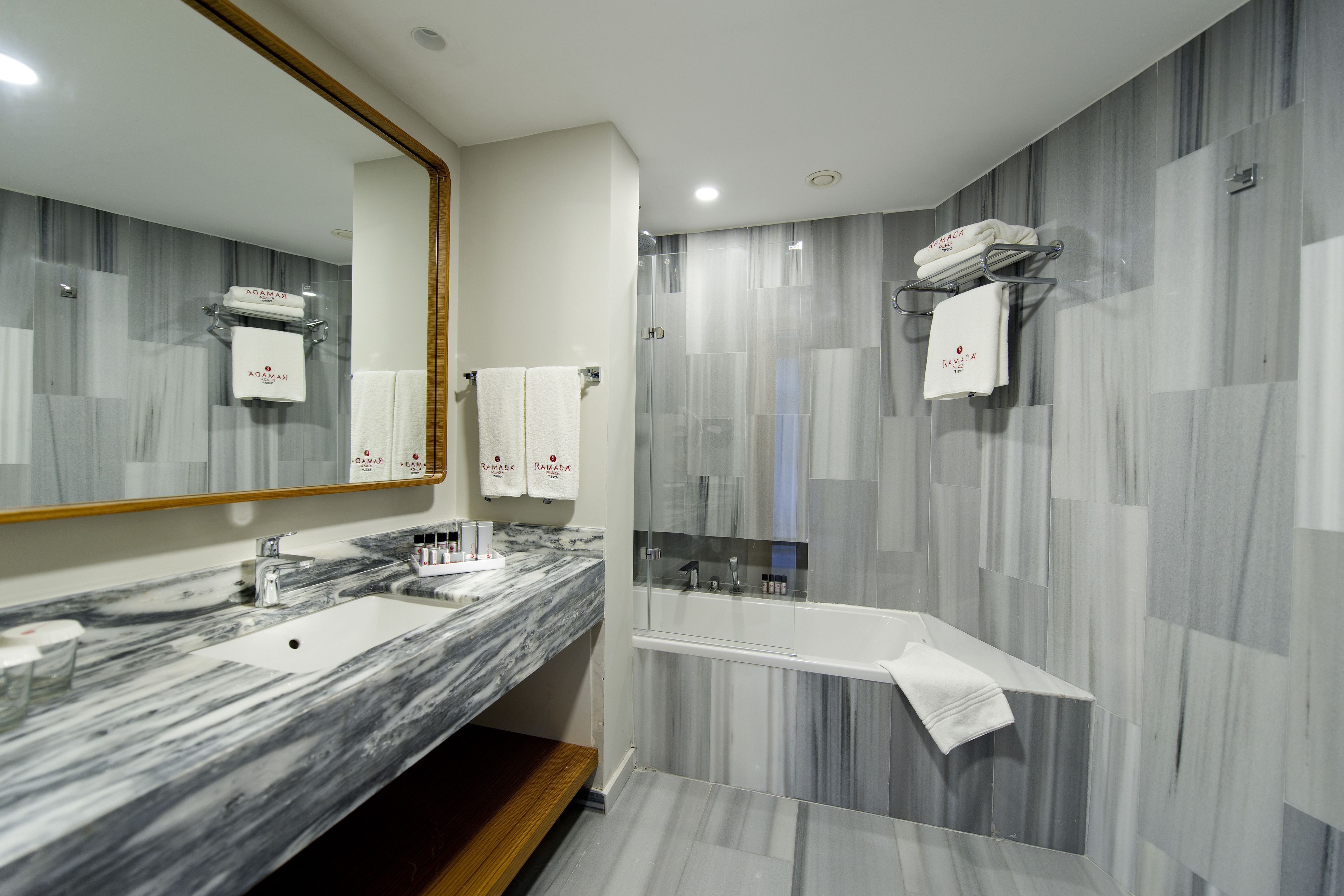 A modern bathroom with a marble vanity, a large mirror, a shower area, and a towel rack.