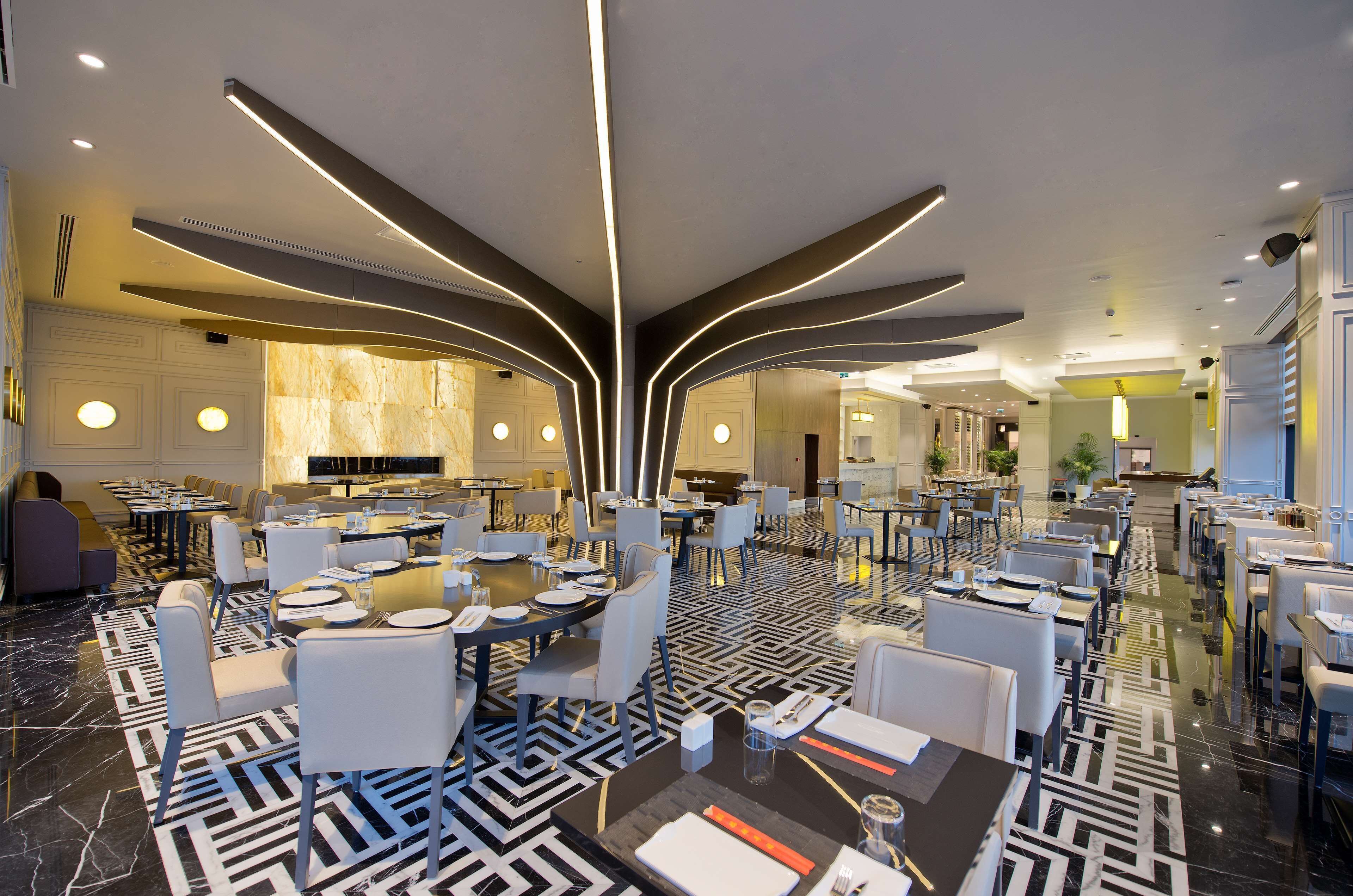 Un comedor de hotel moderno con suelo de estampado geométrico, mobiliario contemporáneo y un elemento de iluminación central.