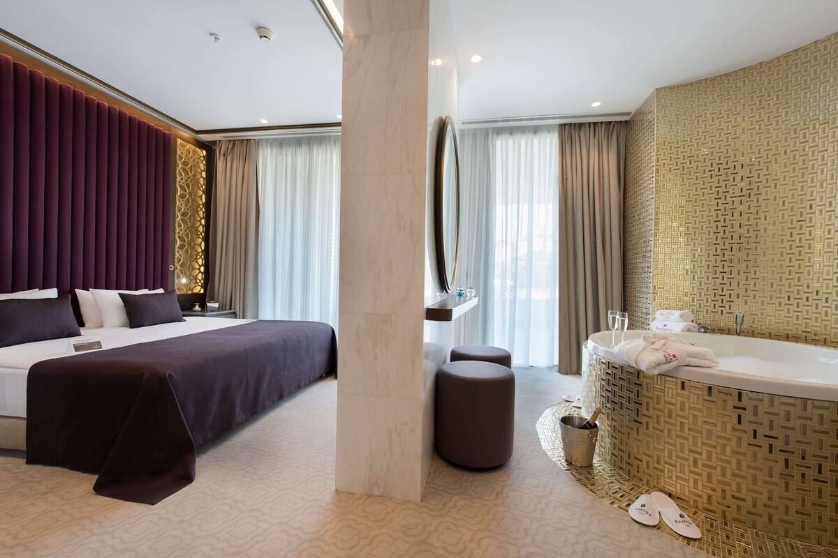 Une chambre d’hôtel moderne dotée d’un grand lit, d’un coin salon séparé, d’une baignoire et d’un minibar.