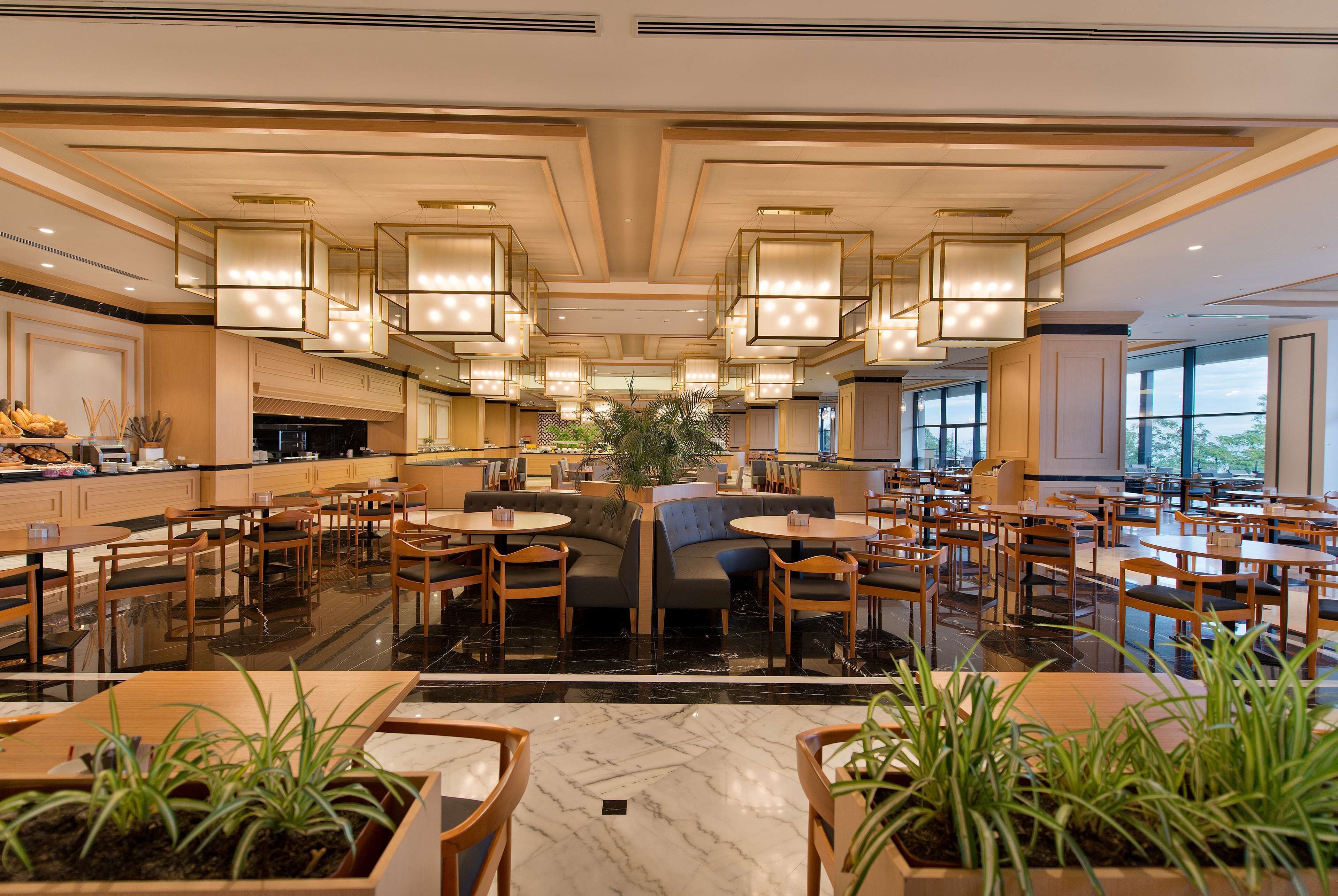 A spacious hotel lobby with multiple seating areas, a central plant, and a modern ceiling design.