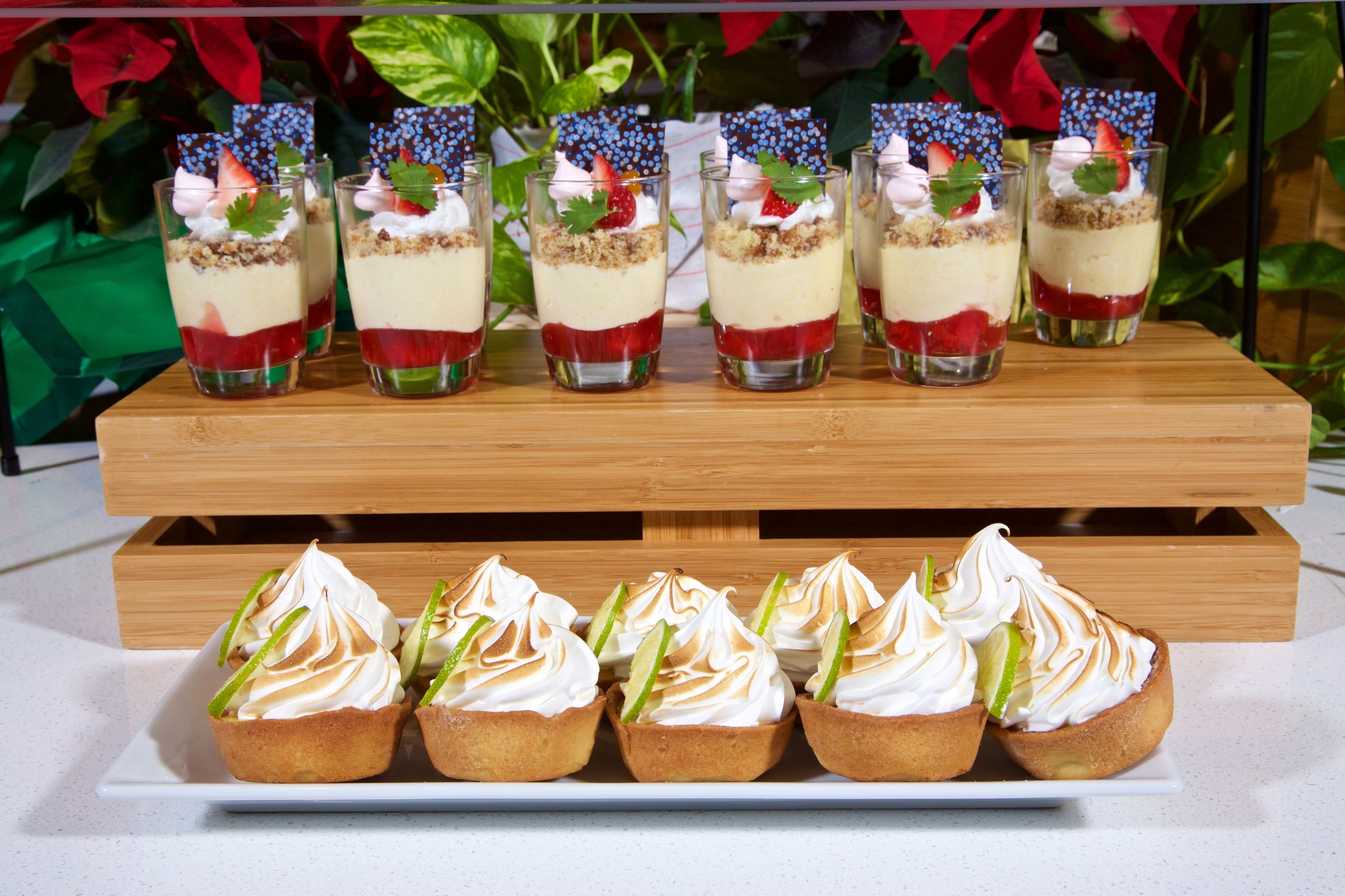 A dessert display with layered parfaits and meringue-topped cupcakes on a wooden stand.
