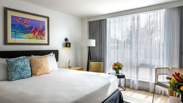 A hotel room with a large bed, a desk, a chair, a window with curtains, and a painting on the wall. - Warwick Paradise Island- All Inclusive- Adults Only (Paradise Island)