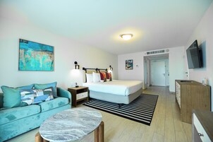 Una habitación de hotel moderna con una cama, un sofá, una mesita de café, un cuadro y un televisor.