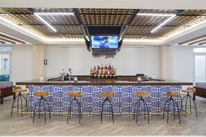 A bar area with a patterned tile backsplash, a flat-screen TV mounted on the ceiling, and a bar counter with stools.