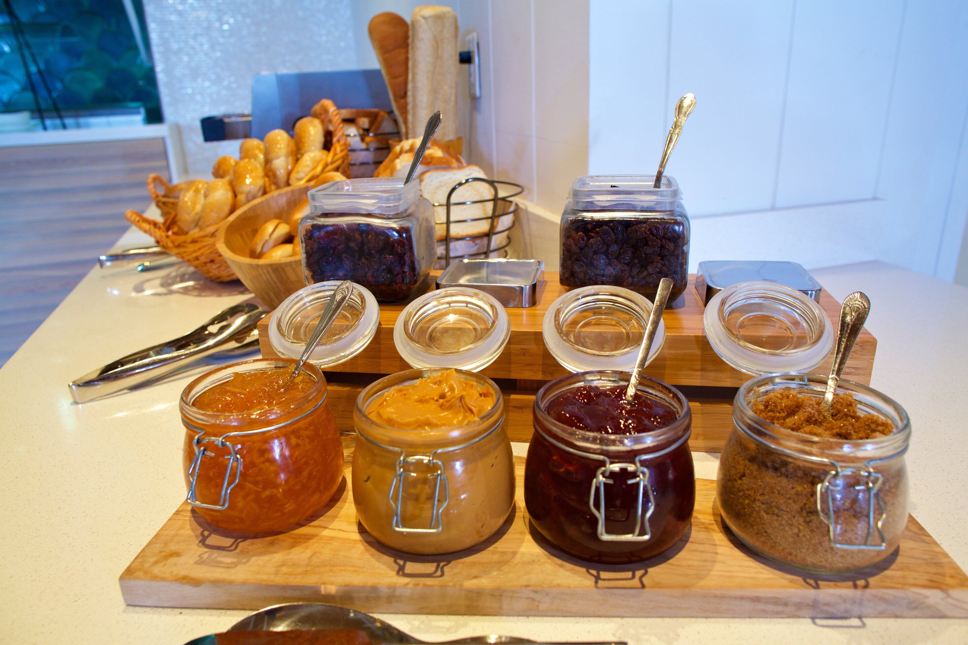 A breakfast buffet with various jams and spreads, a basket of croissants, and a loaf of bread.