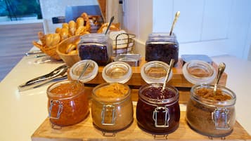 A breakfast buffet with various jams and spreads, a basket of croissants, and a loaf of bread.
