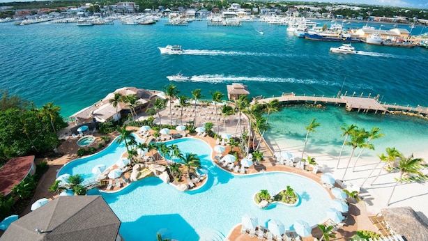 A resort with a large pool area, a dock, and boats in the background. - Warwick Paradise Island- All Inclusive- Adults Only (Paradise Island)