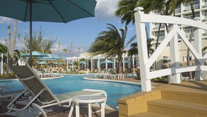 A pool area with lounge chairs and umbrellas, surrounded by palm trees and a building with balconies. - Warwick Paradise Island- All Inclusive- Adults Only (Paradise Island)