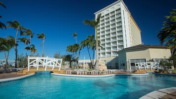 A hotel with a large pool surrounded by palm trees and a white building with balconies.
