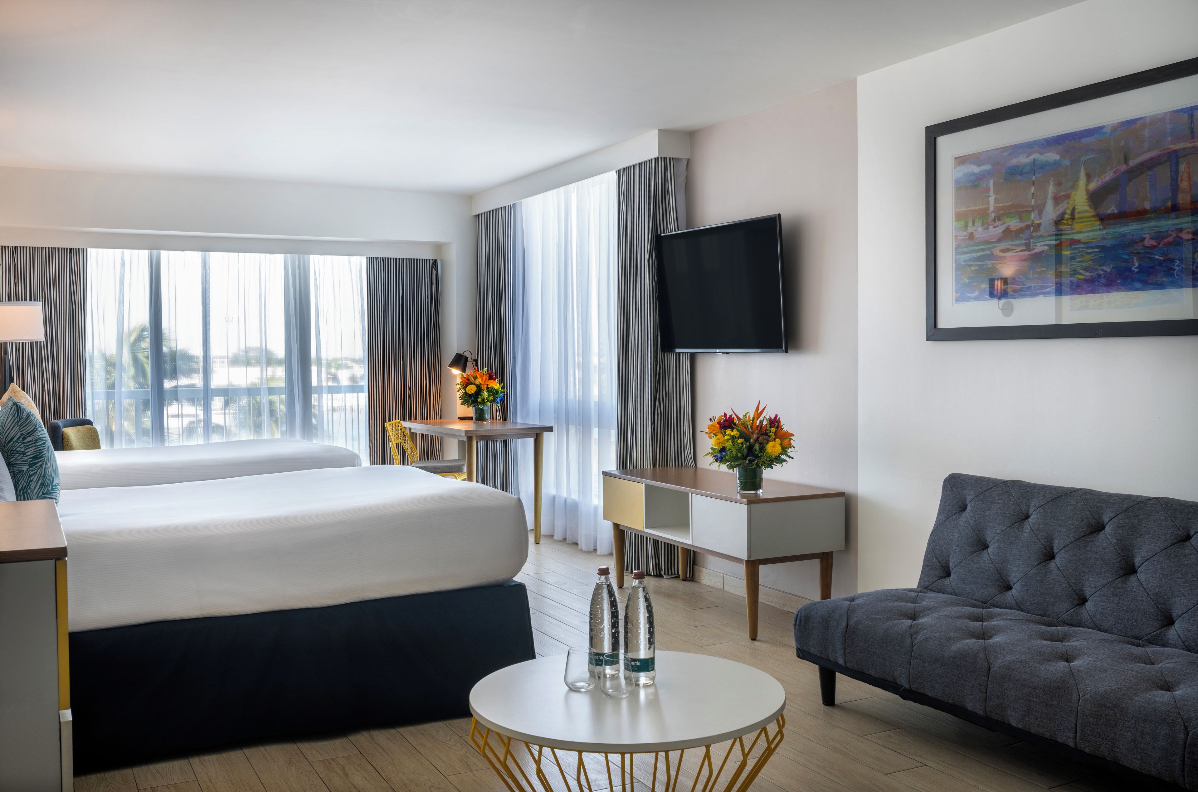 Et hotelværelse med seng, skrivebord, sofa, fjernsyn og et billede på v æggen.