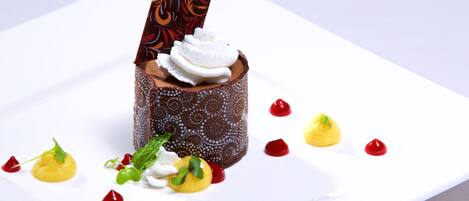A dessert on a white plate with chocolate, white cream, and garnishes.