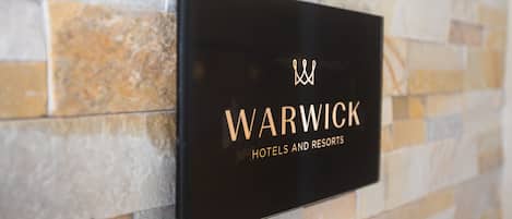 A black sign with gold lettering that reads "WARWICK HOTELS AND RESORTS" mounted on a stone wall.