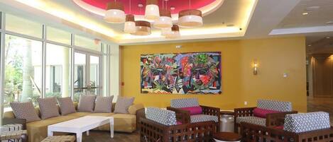 A modern lobby with a large window, a colorful abstract painting, and a seating area with patterned cushions.