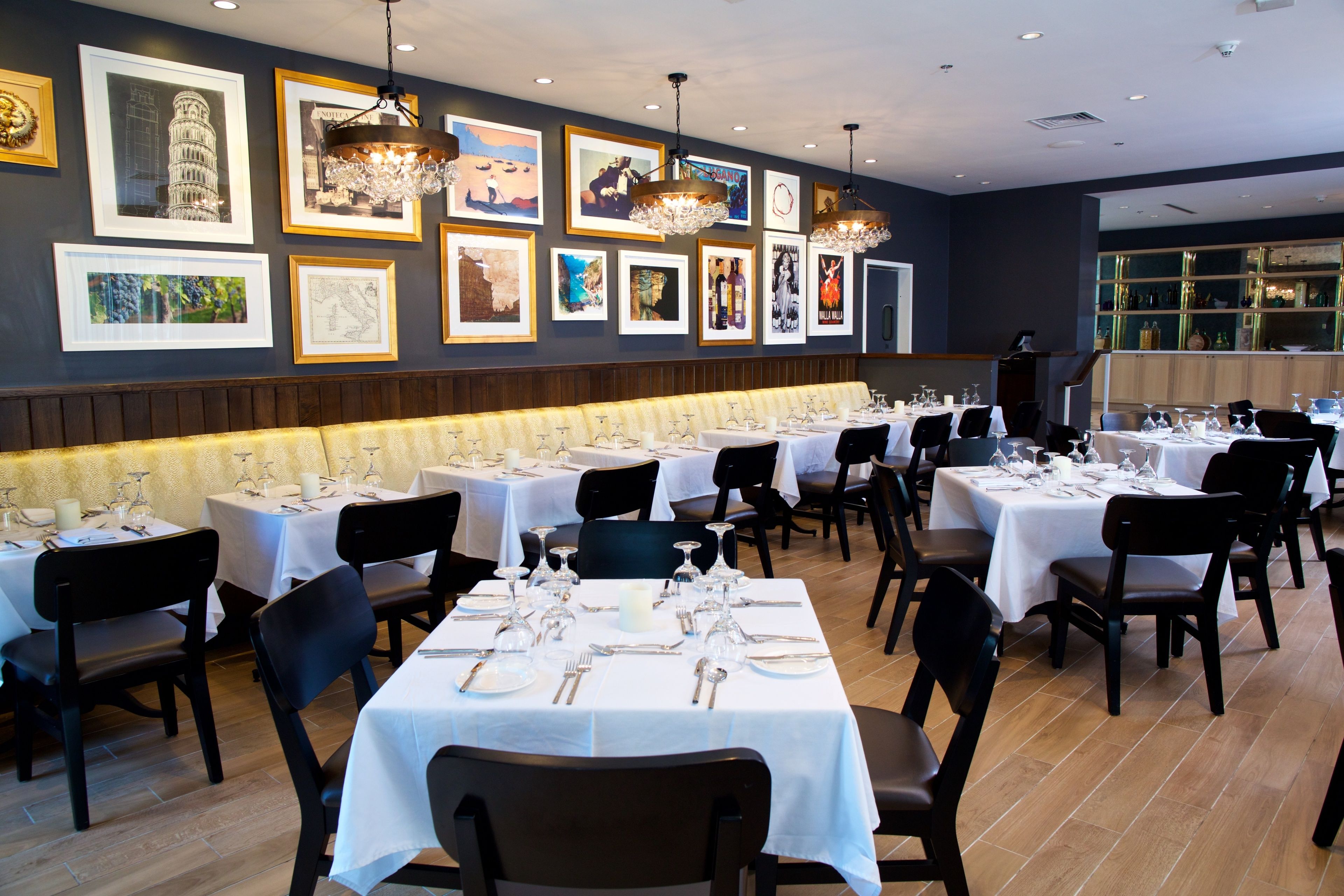 Un restaurante con varias mesas dispuestas para comer, obras de arte en las paredes y una zona de bar visible a través del cristal.