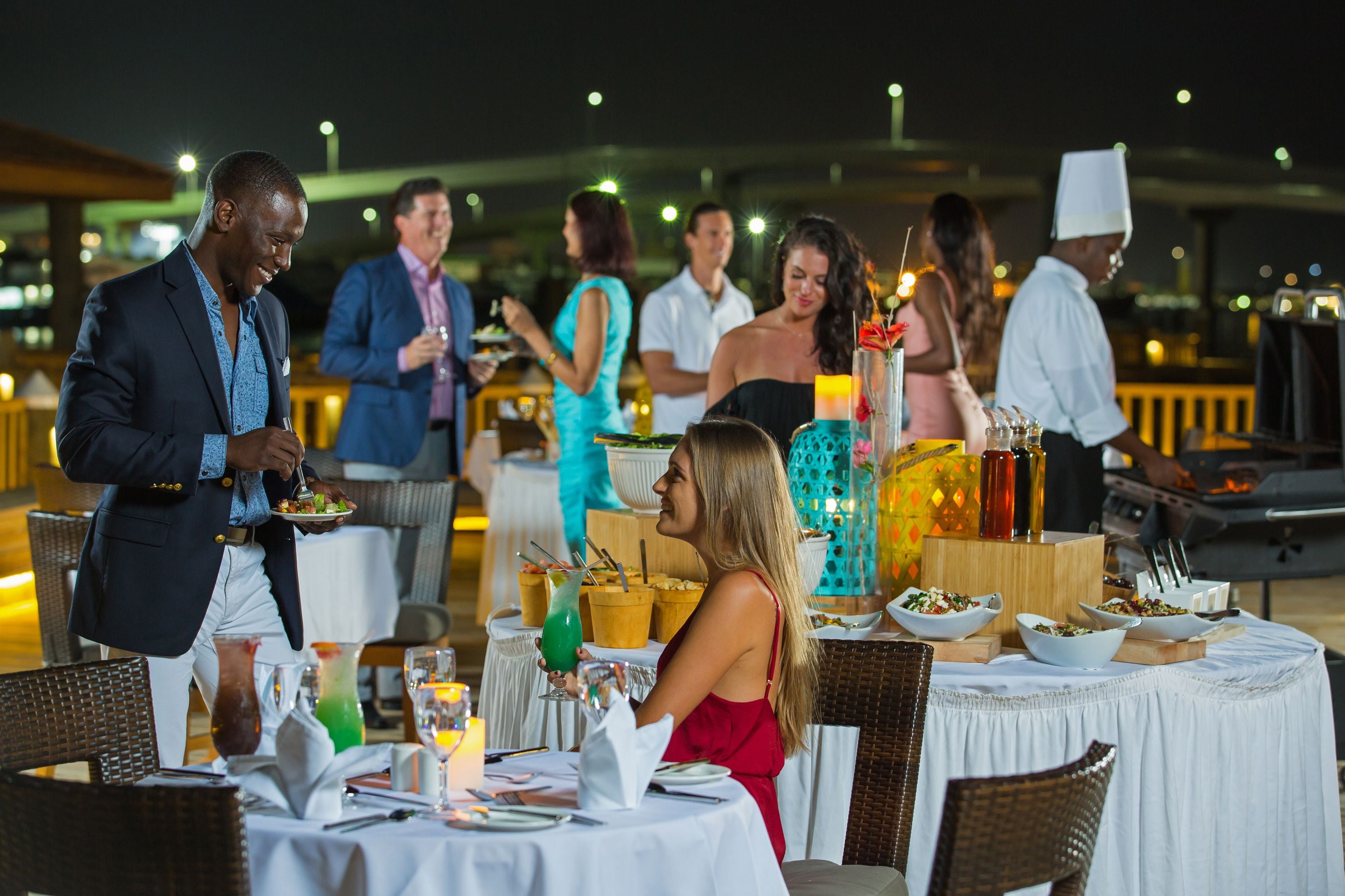 A restaurant setting with round tables, wicker chairs, and a variety of dishes and drinks.