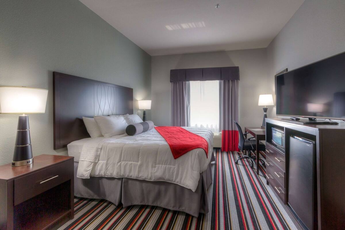 A hotel room with a bed, bedside lamps, a desk with a flat-screen TV, a microwave, and a refrigerator.